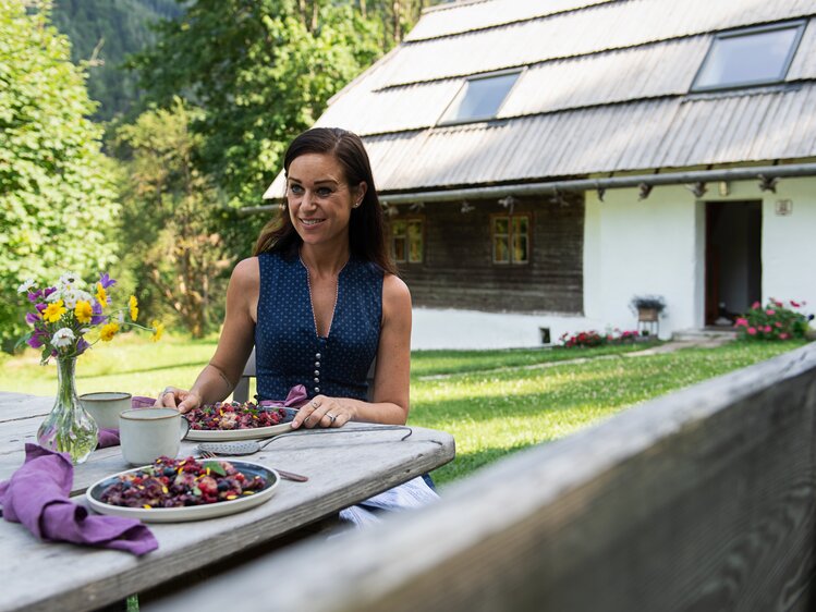 Cooking Catrin mit Himbeerdessert und Almhütte im Hintergrund | © Carletto Photography / Urlaub am Bauernhof Kärnten