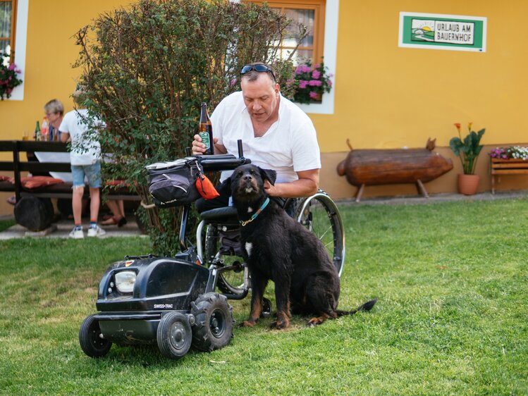 Mann im Rollstuhl streichelt den Hofhund | © Urlaub am Bauernhof / Daniel Gollner