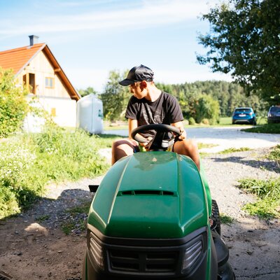 Junge sitzt am Rasenmähertraktor und Blickt nach hinten | © Urlaub am Bauernhof Kärnten / Daniel Gollner