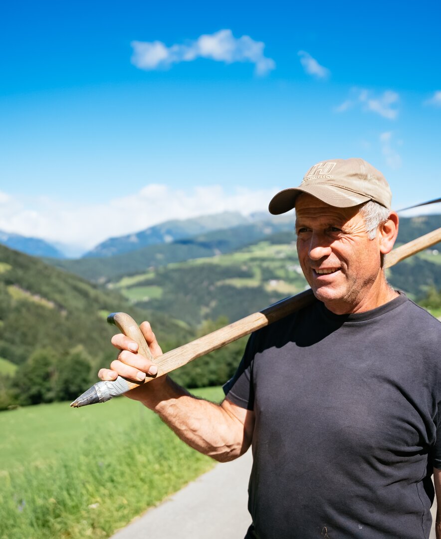 Bauer hat die Sense geschultert und steht auf der Straße | © Urlaub am Bauernhof Kärnten / Daniel Gollner