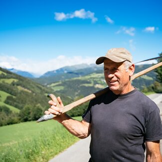 Bauer hat die Sense geschultert und steht auf der Straße | © Urlaub am Bauernhof Kärnten / Daniel Gollner