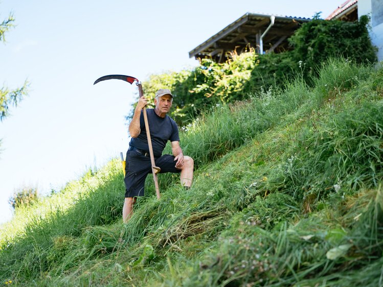 Bauer steht mit der Sense am Hang | © Urlaub am Bauernhof Kärnten / Daniel Gollner