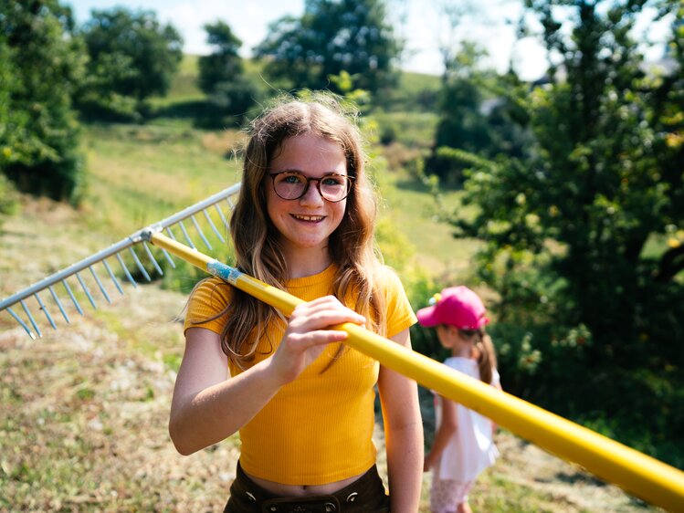 Mädchen mit dem Rechen auf der Wiese | © Urlaub am Bauernhof Kärnten / Daniel Gollner