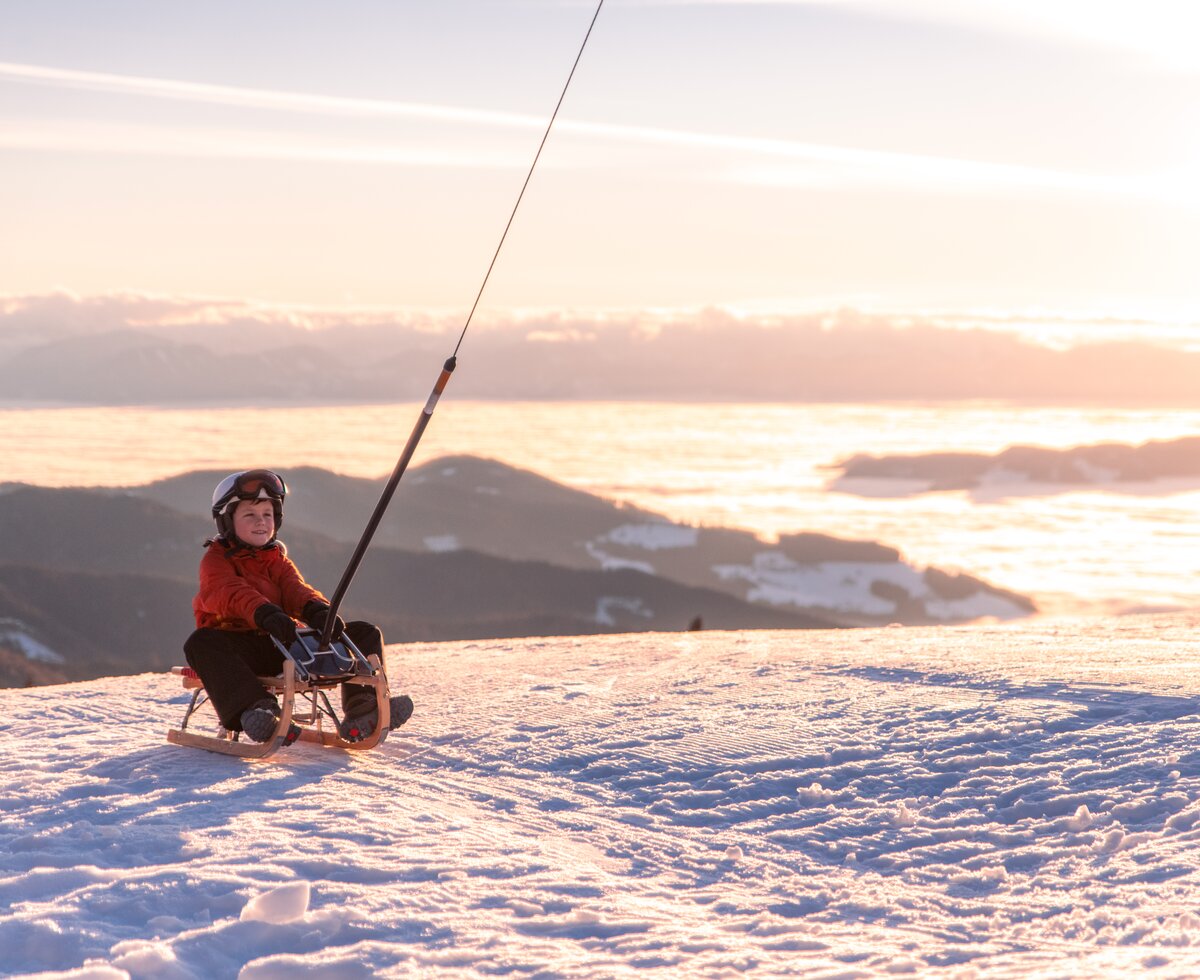 Kind auf Schlitten im Abendlicht im Schnee | © Michael Stabentheiner / Tourismusregion Mittelkärnten