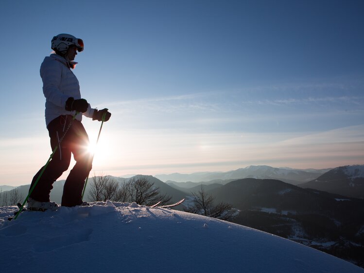 Skifahrerin steht auf Gipfel bei Sonnenaufgang | © Niederösterreich Werbung / schwarz-koenig.at