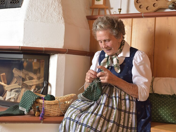 Oma im Dirndl strickt Socken am Kachelofen | © Urlaub am Bauernhof Oberösterreich / Harald Puchegger