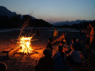 Gäste sitzen am Lagerfeuer im Dunkeln und grillen | © Bio-Bergbauernhof Weger