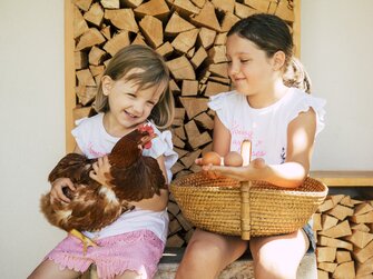 Zwei Mädchen sitzen mit einem Huhn und Eiern auf der Hausbank | © Urlaub am Bauernhof / Oststeiermark Tourismus / Bernhard Bergmann