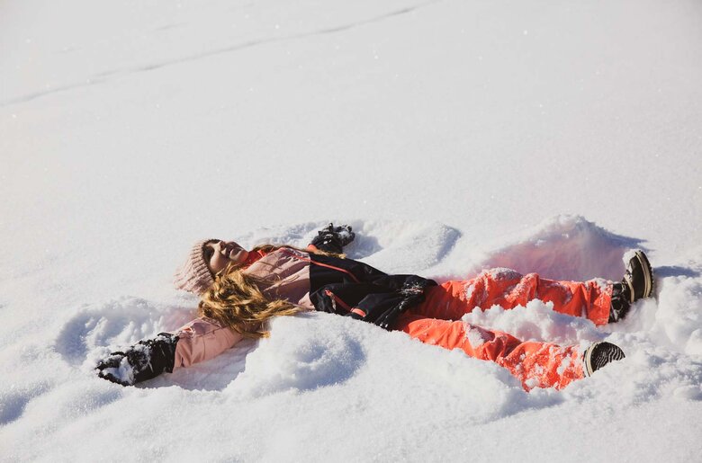 Mädchen mit buntem Schianzug macht Schneeengel | © Urlaub am Bauernhof / Pascal Baronit