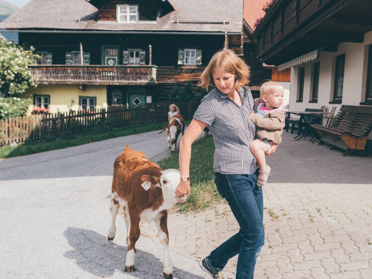 Bäuerin Kathrin Röck vom Grußberggut in Bad Hofgastein hält ihr Baby am Arm und führt ein Kalb über den Hof | © Urlaub am Bauernhof im SalzburgerLand / Daniel Gollner