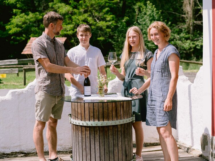 Familie Monschein mit Weingläsern am Holzfass-Tisch stehend | © Urlaub am Bauernhof Steiermark / Familie Monschein