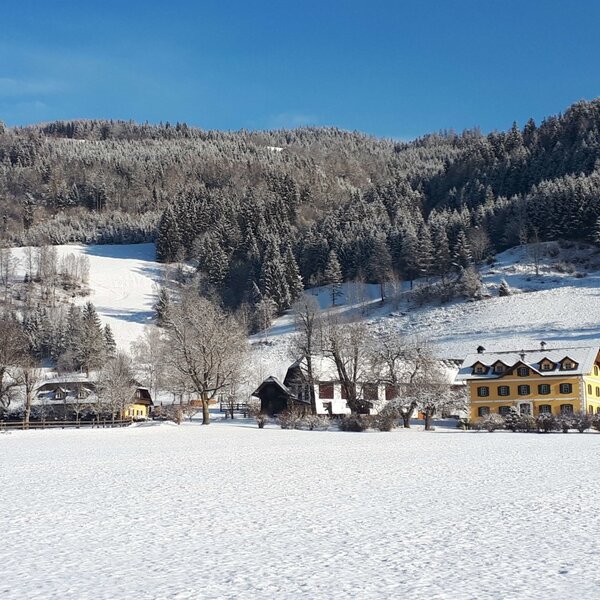 Außenansicht des Bauernhofs Fuggerhof im Winter, mit schneebedeckten Feldern und bewaldeten Hängen. Außenansicht des Bauernhofs Fuggerhof im Winter, mit schneebedeckten Feldern und bewaldeten Hängen.